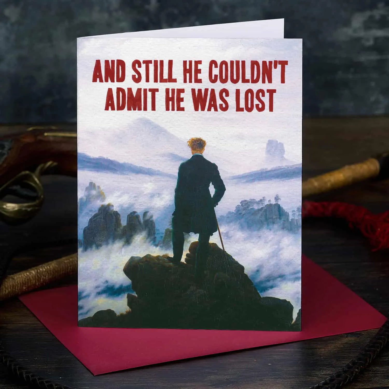 Greeting card with a silhouette of a person on a rocky outcrop and text 'And still he couldn't admit he was lost' on a dark background.