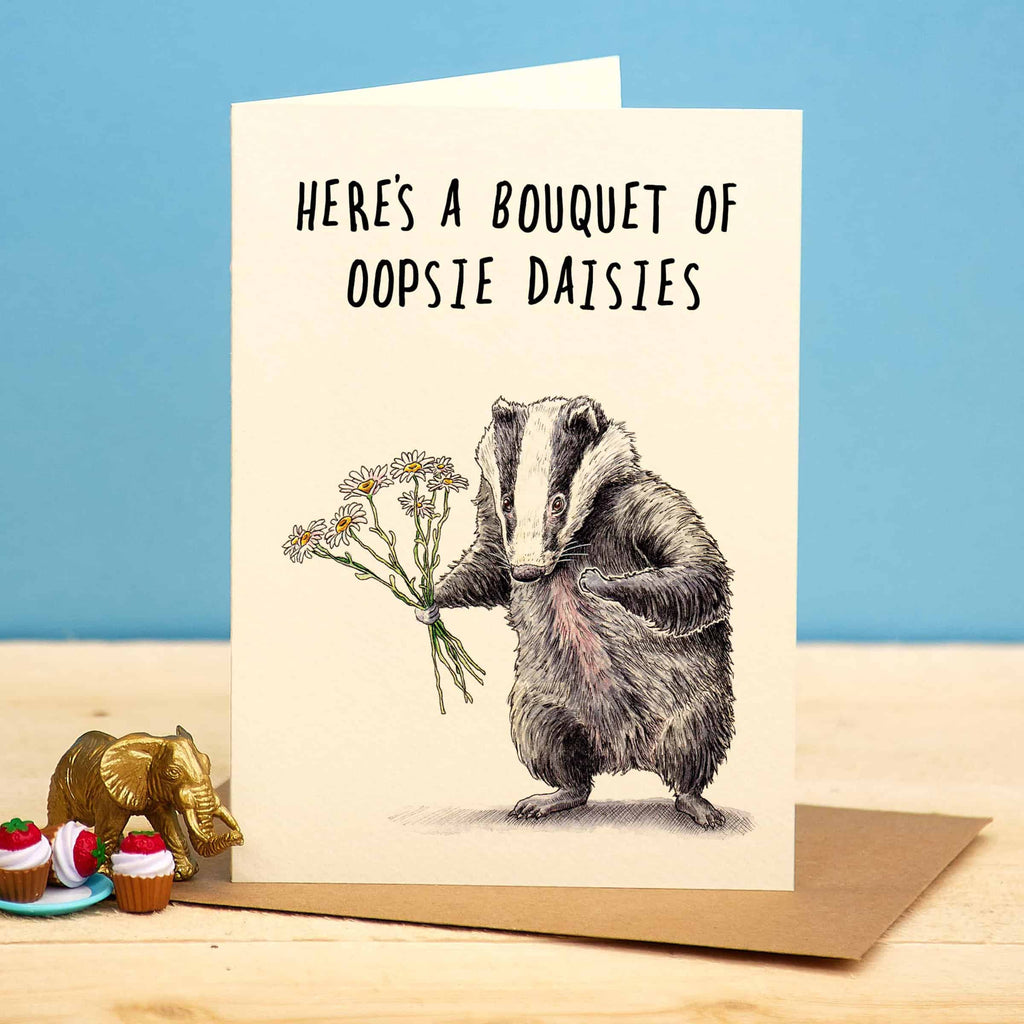 Greeting card with a badger holding flowers and text on a wooden surface with a blue background
