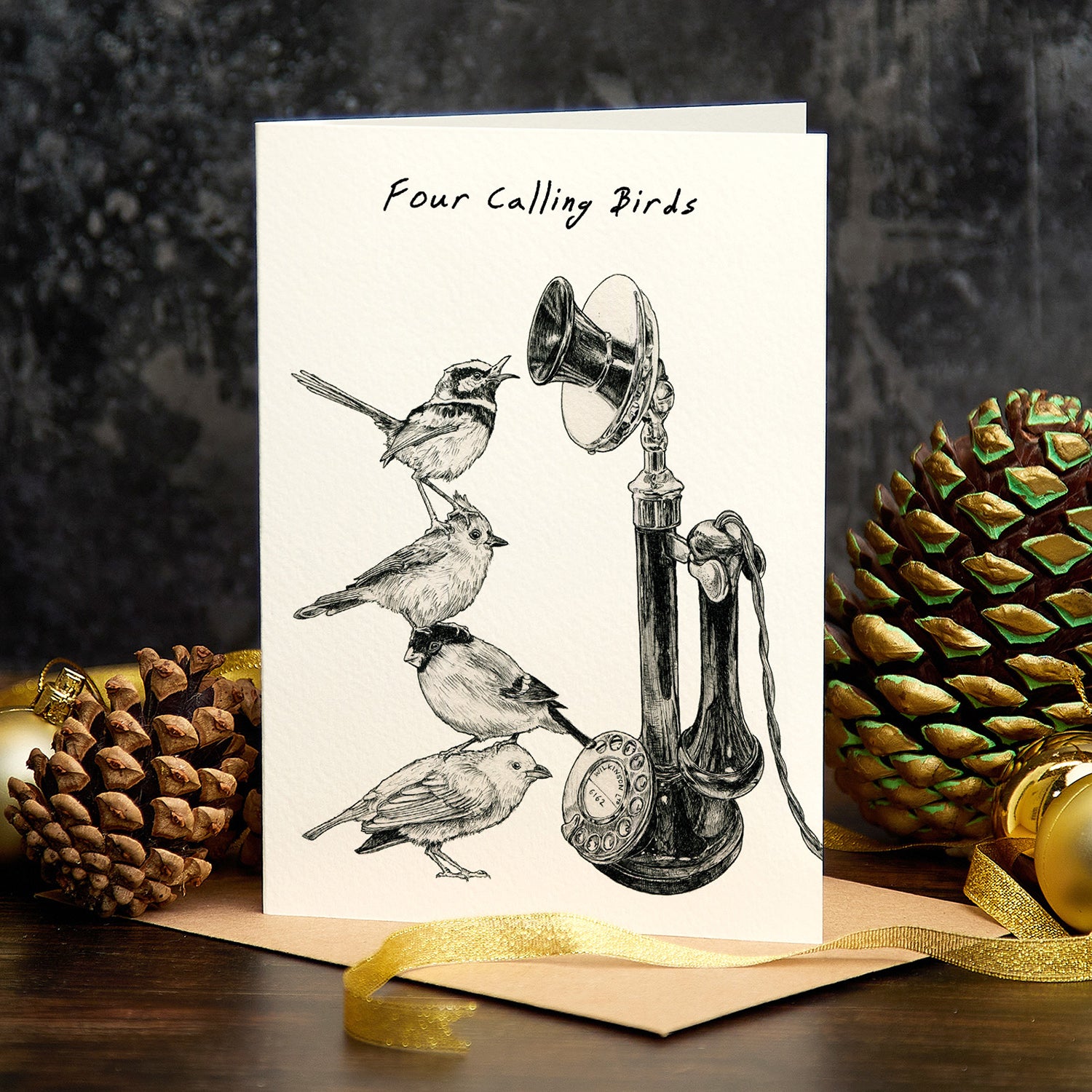 Greeting card with illustration of four birds and a bell, surrounded by pine cones and a gold ribbon.