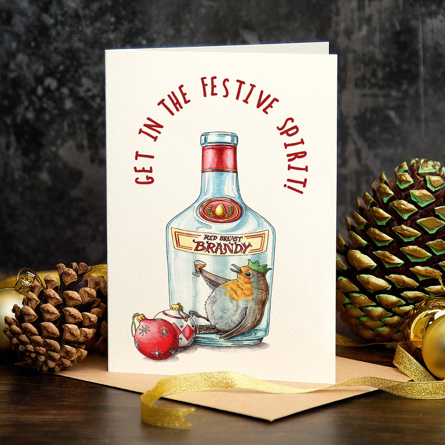 Greeting card with brandy bottle illustration and festive text, surrounded by pine cones and gold ribbon.