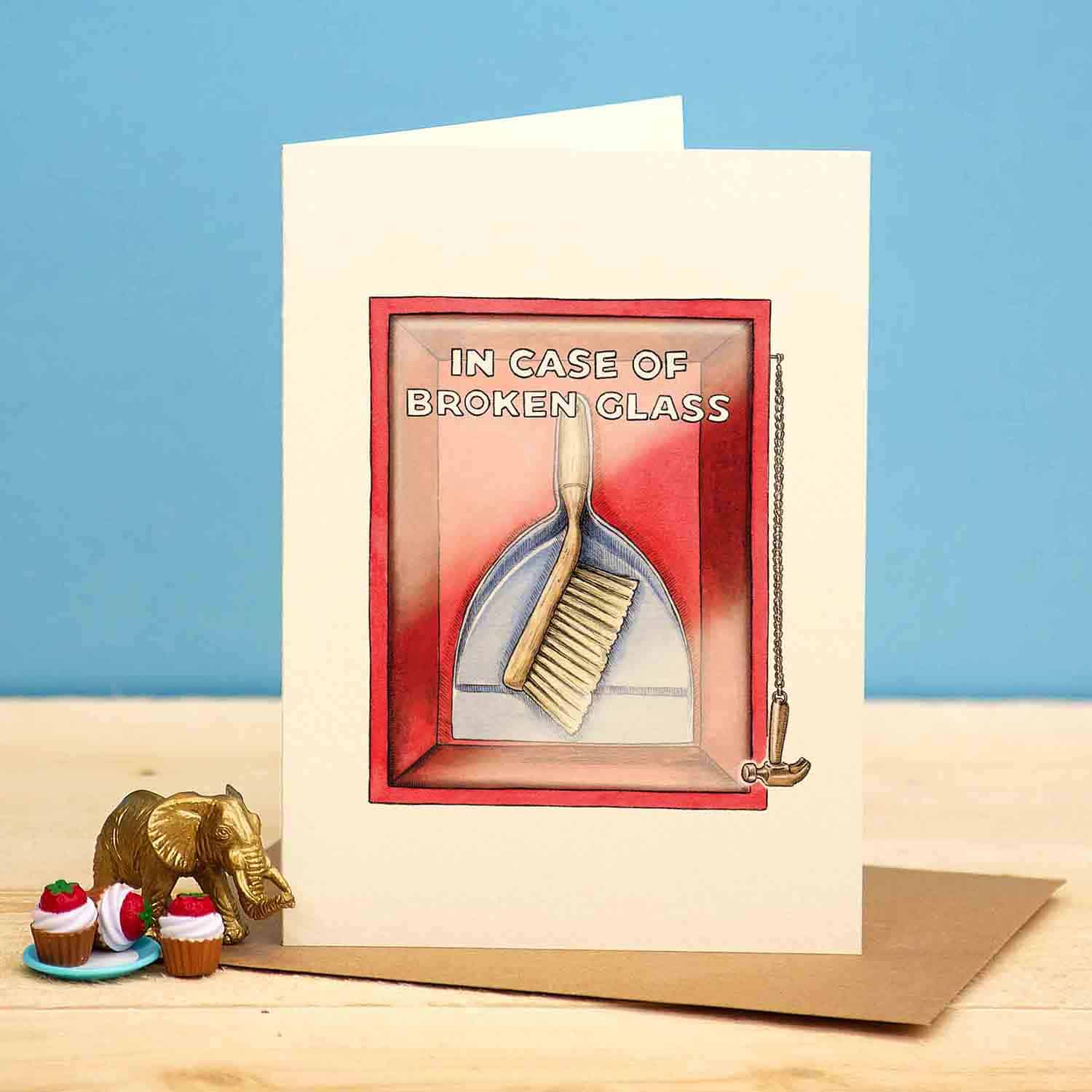 Greeting card with a humorous illustration of a brush and pan and text 'In case of broken glass' on a blue background.