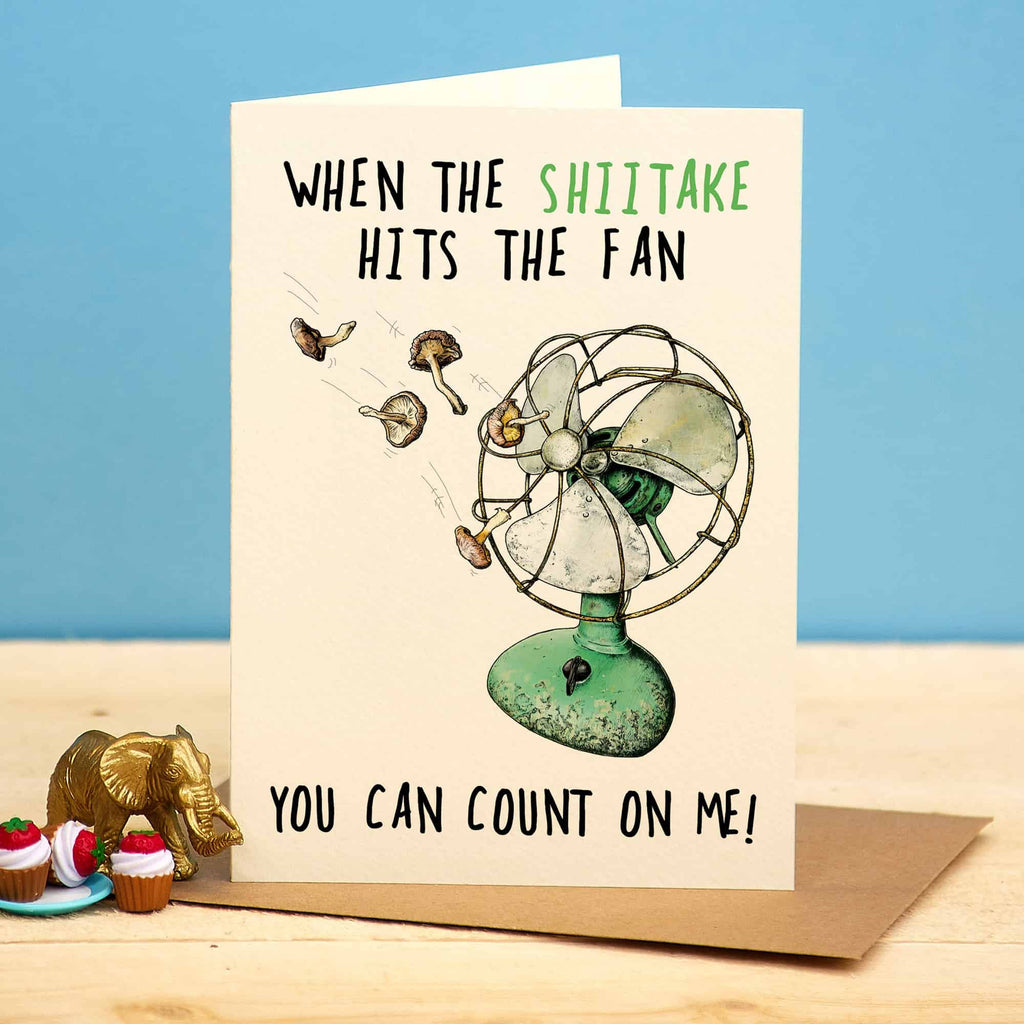 Card with a vintage fan illustration and humorous text on a wooden surface with a blue background