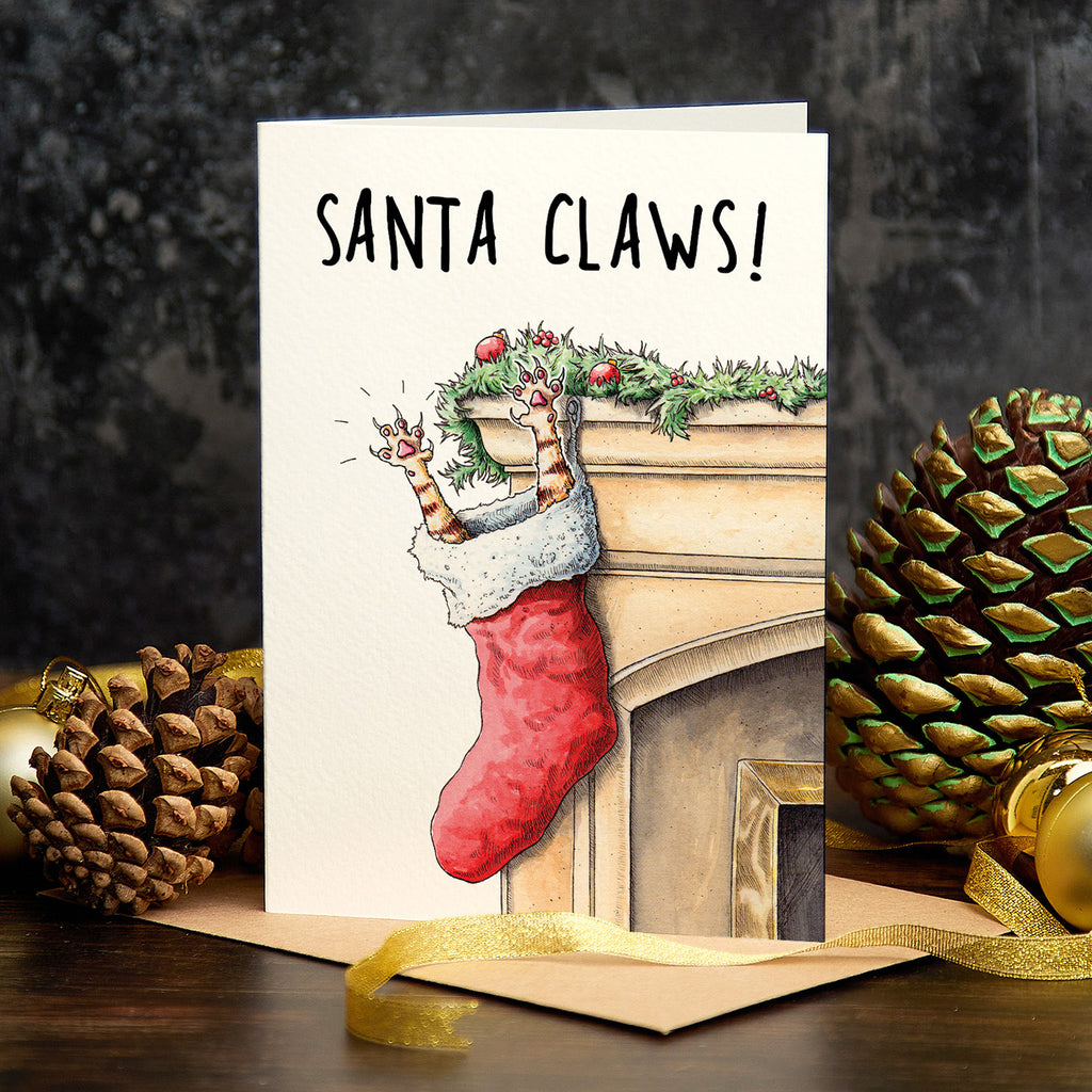 Christmas card with red stocking and 'Santa Claws!' text, surrounded by pine cones and gold ribbon.
