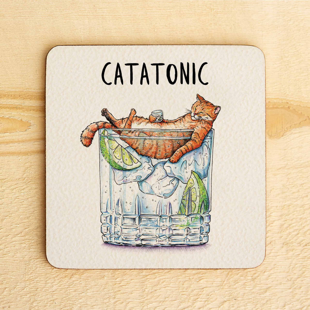 Coaster with a cat in a cocktail glass and 'Catatonic' text on a wooden surface
