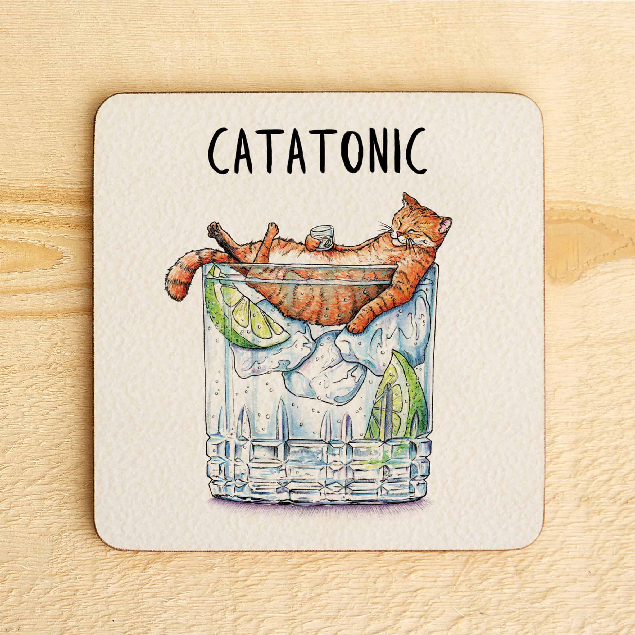 Coaster with a cat in a cocktail glass and 'Catatonic' text on a wooden surface