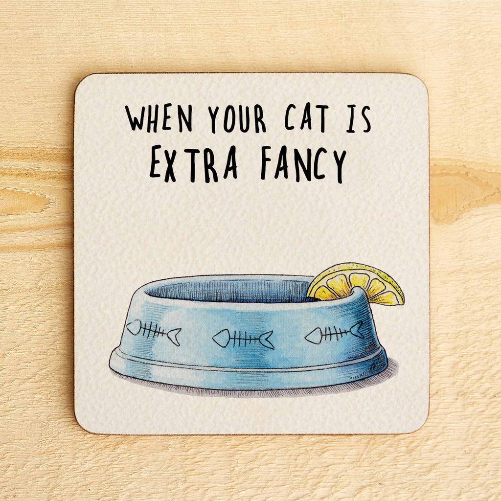 Coaster with a blue cat bowl illustration and text 'When your cat is extra fancy' on a wooden surface.