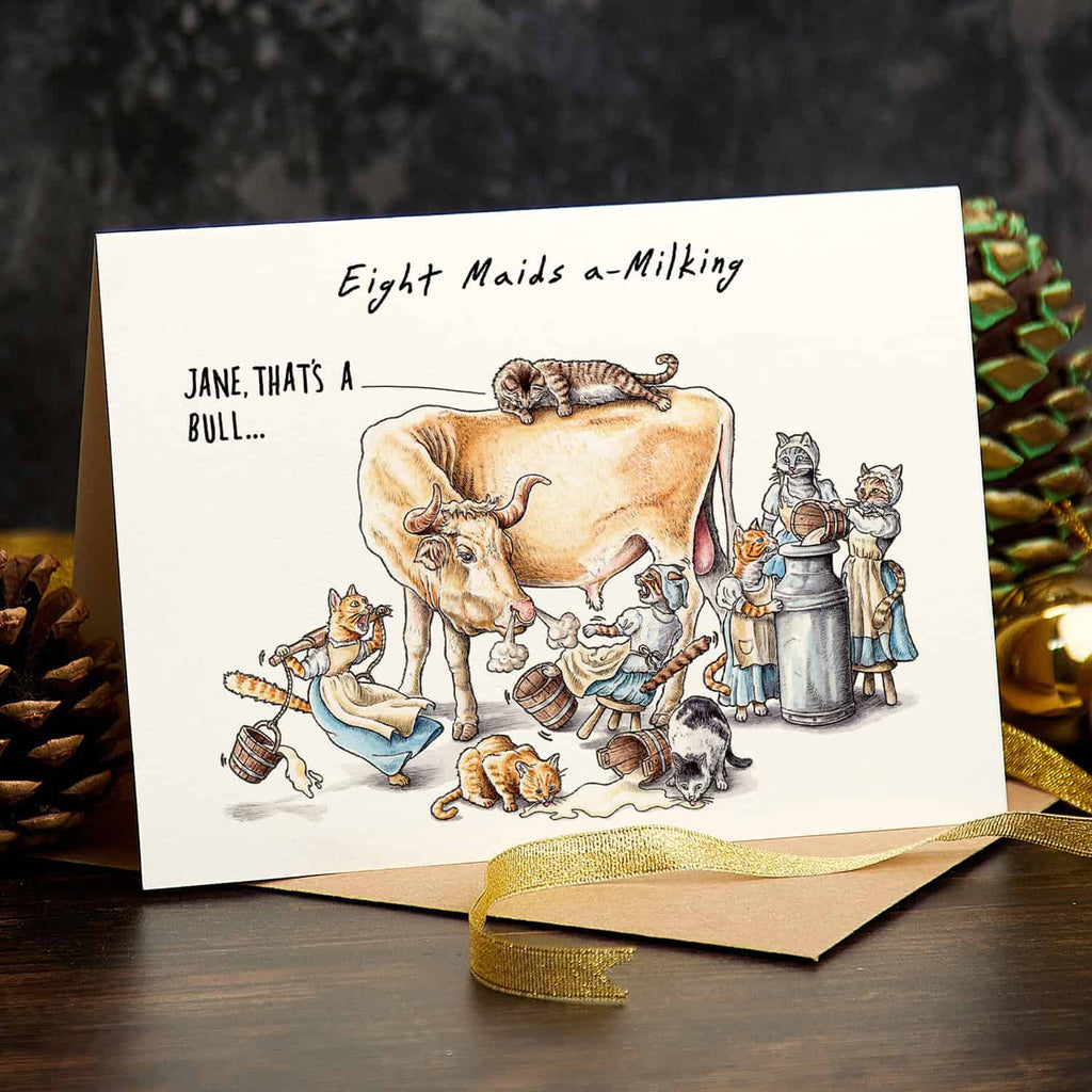 Card with illustration of a cow and eight maids a-milking, with a gold ribbon and pinecones in the background.