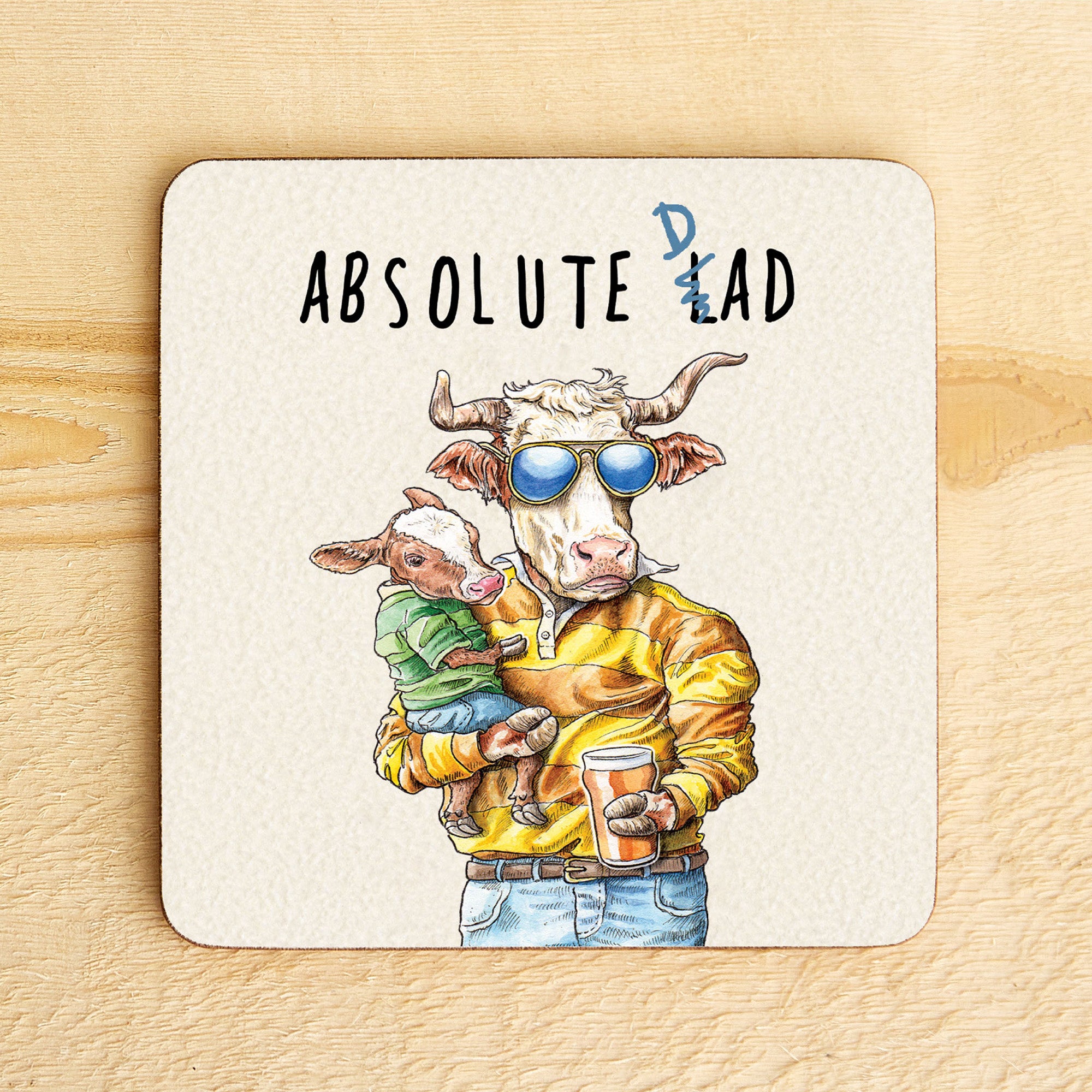 Coaster with illustration of a cow holding a calf and text 'Absolute Dad' on a wooden surface