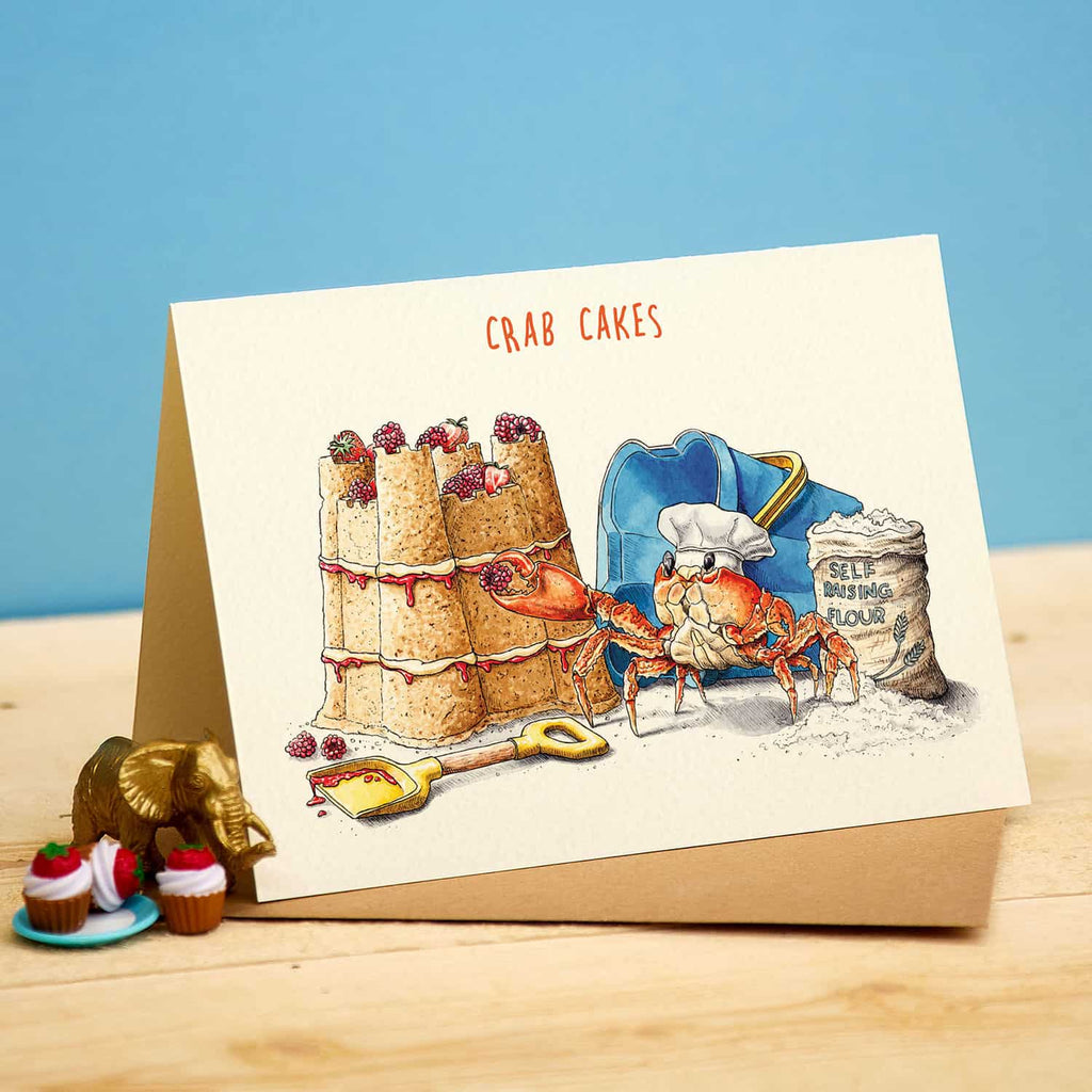 Card with illustration of crab cakes and a chef crab, on a wooden surface with a blue background.