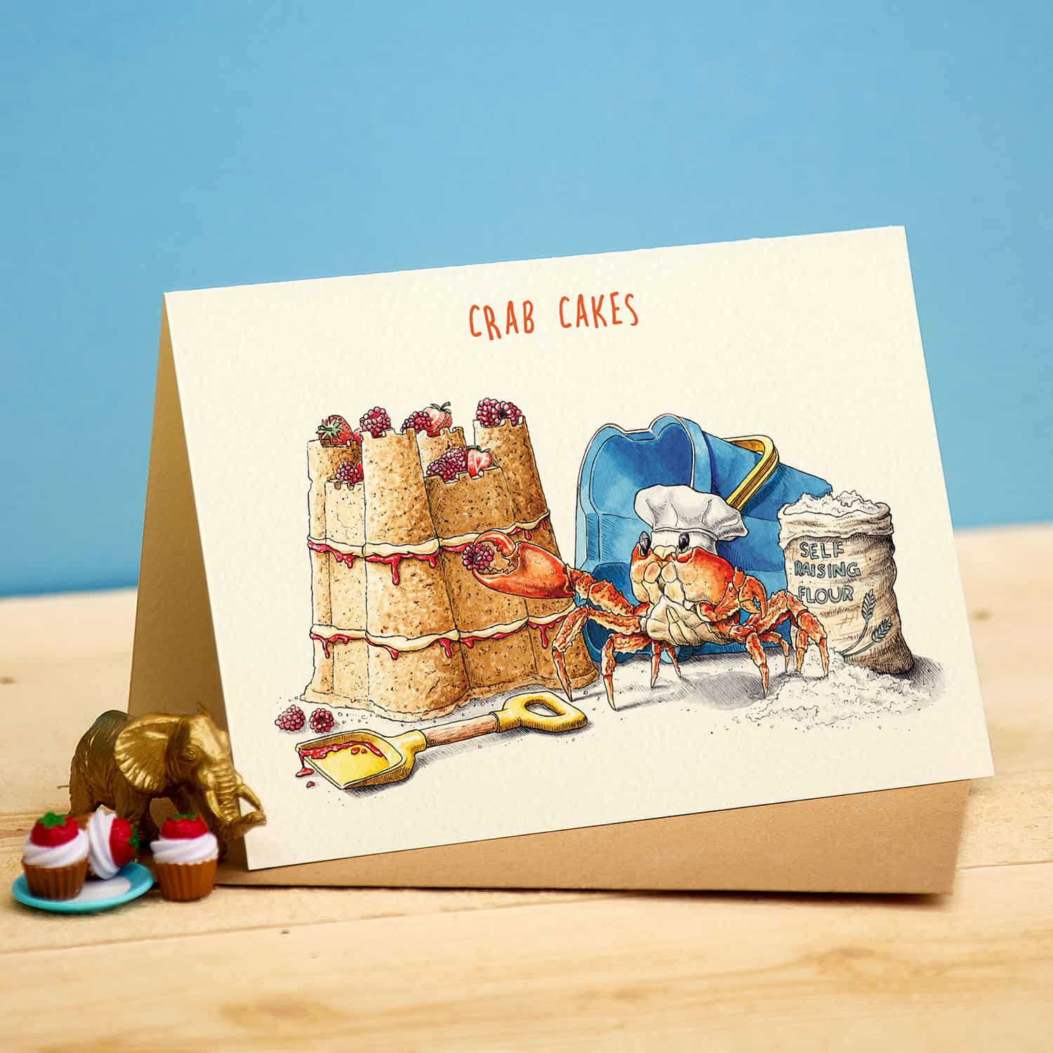Card with illustration of crab cakes and a chef crab, on a wooden surface with a blue background.