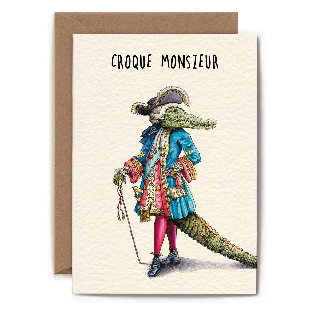 Greeting card with an illustration of a crocodile in formal attire and the text 'Croque Monsieur' on a beige background.