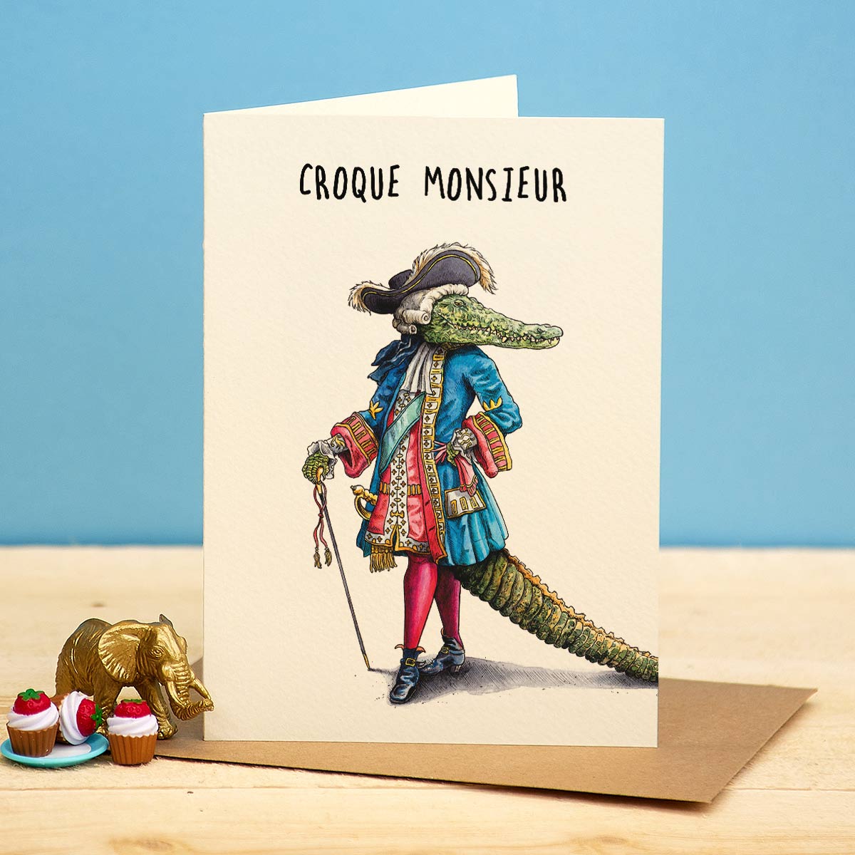 Greeting card with a crocodile in formal attire and 'Croque Monsieur' text on a blue and beige background.