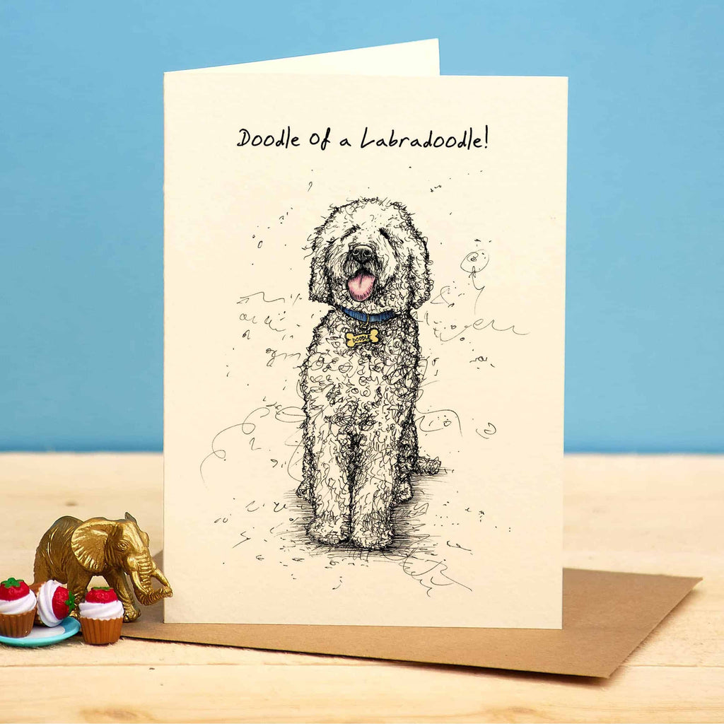 Greeting card with a doodle of a Labradoodle on a wooden surface with decorative items.