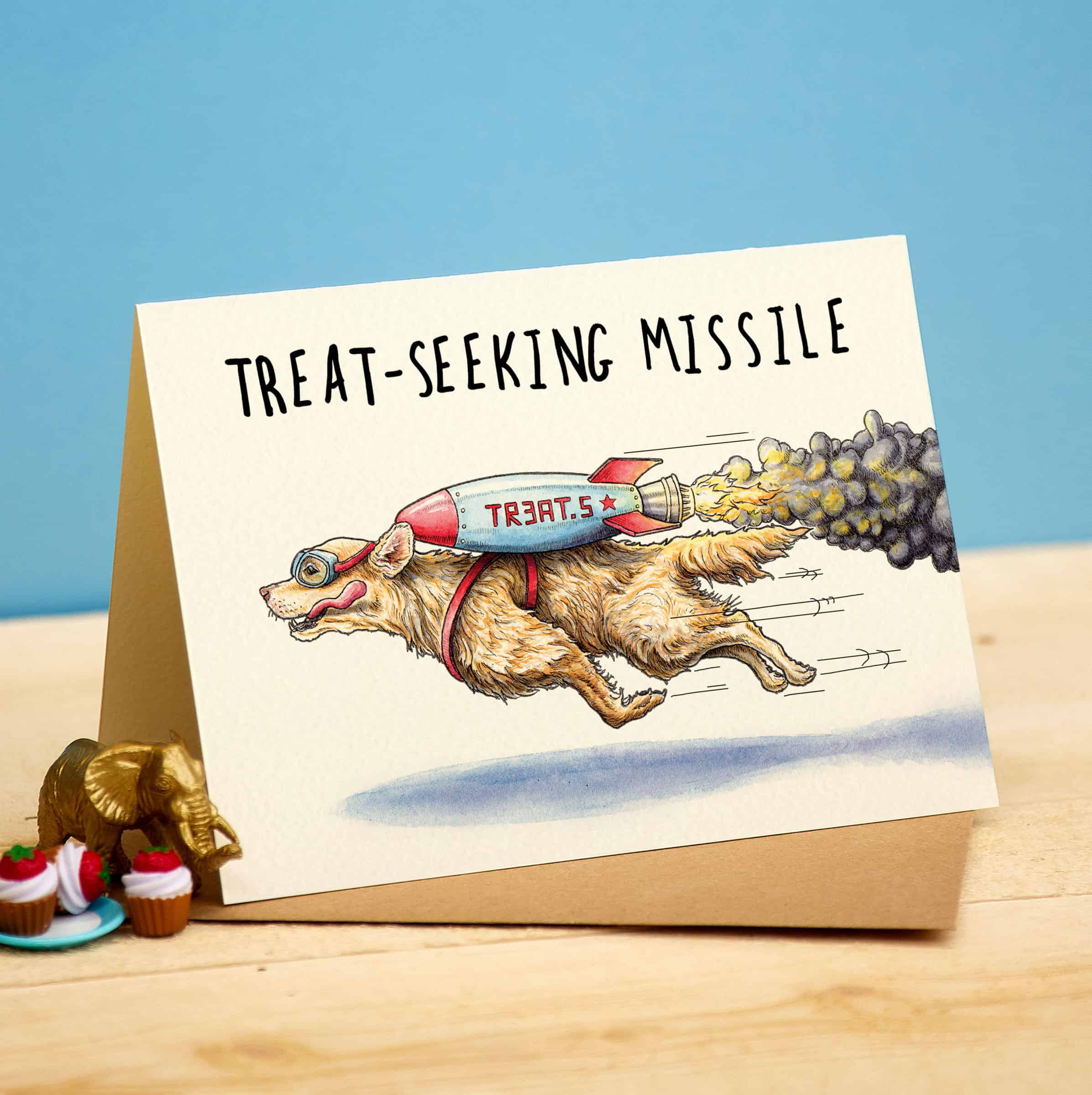 Card with a dog carrying a 'Treat Seeking Missile' on a blue background
