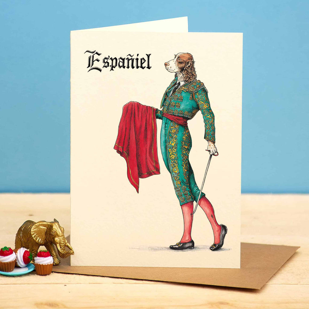 Greeting card with a dog in a formal outfit labeled 'Español' on a wooden surface with a blue background.