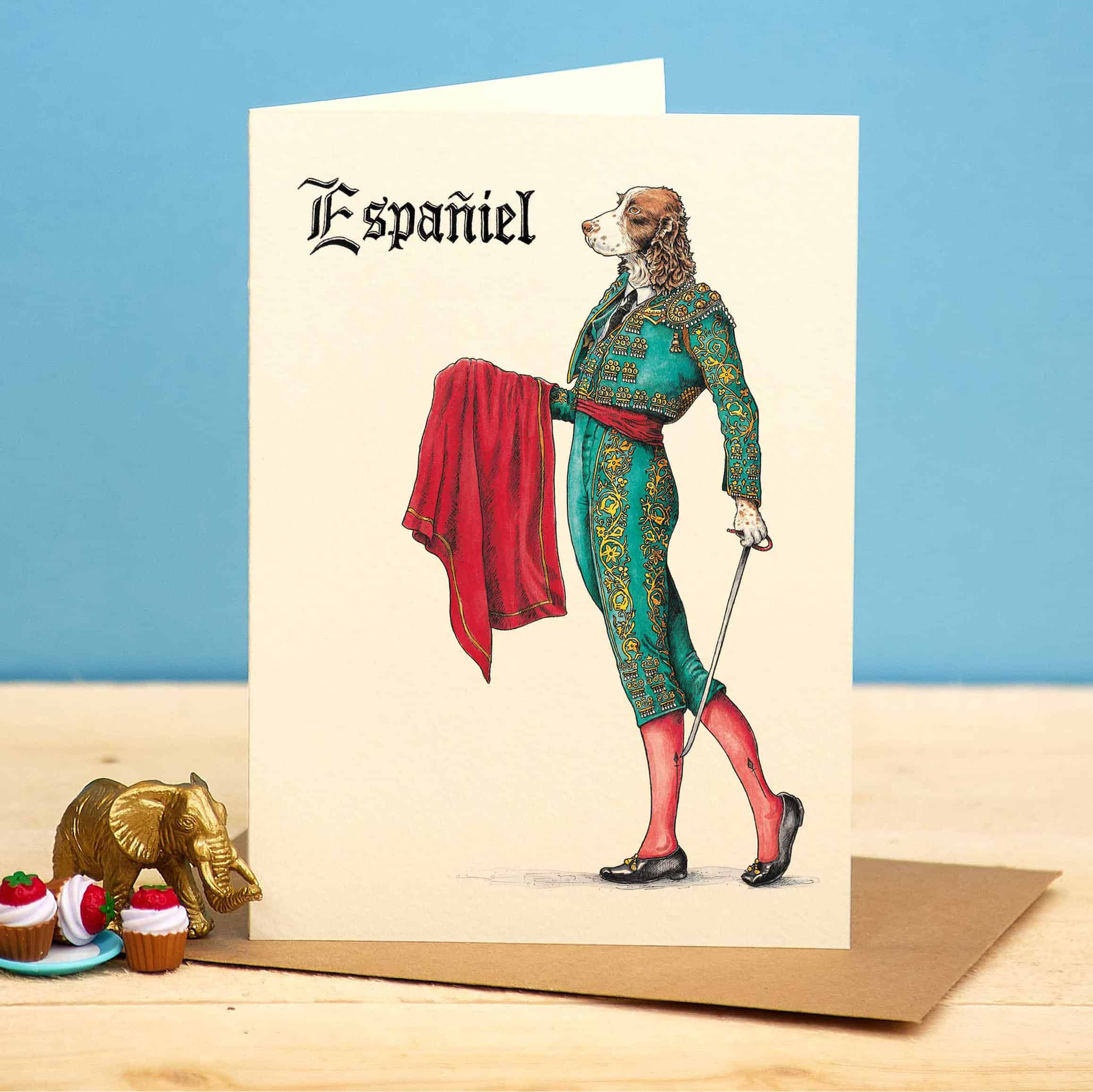 Greeting card with a dog in a formal outfit labeled 'Español' on a wooden surface with a blue background.