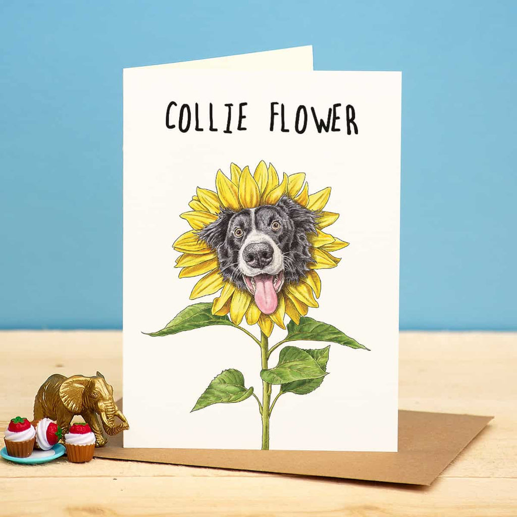 Card with a dog illustration inside a sunflower, on a wooden surface with a blue background.
