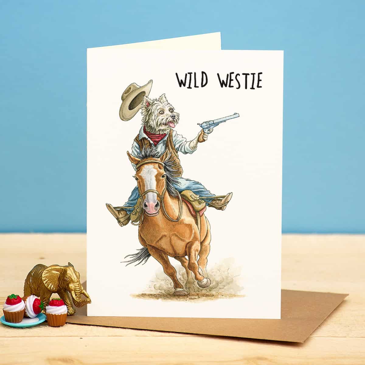 Card with a dog in cowboy attire riding a horse, labeled 'Wild Westie', on a blue background.