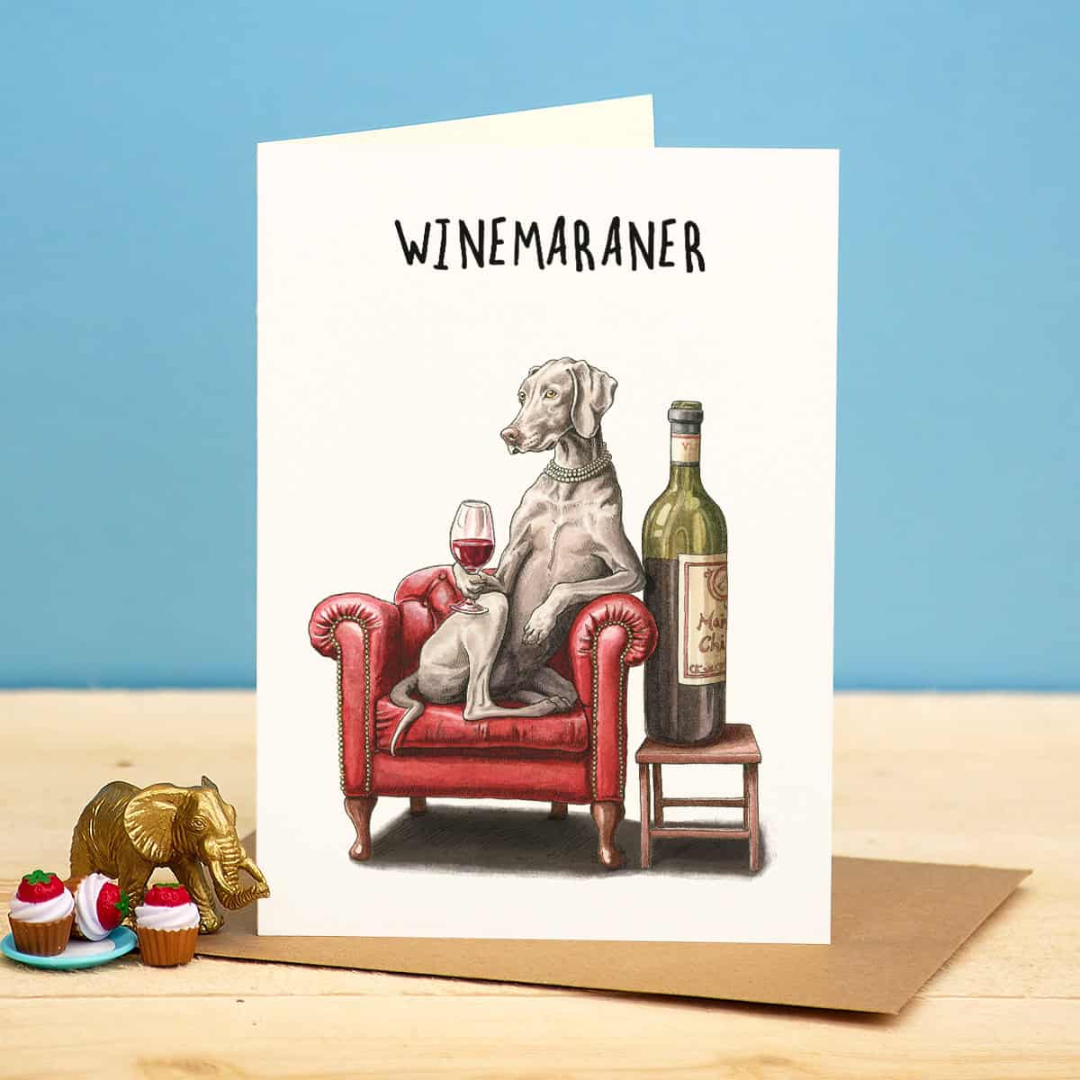 Greeting card with a dog sitting on a red armchair with a wine bottle and glass, labeled 'WINEMARANER'.
