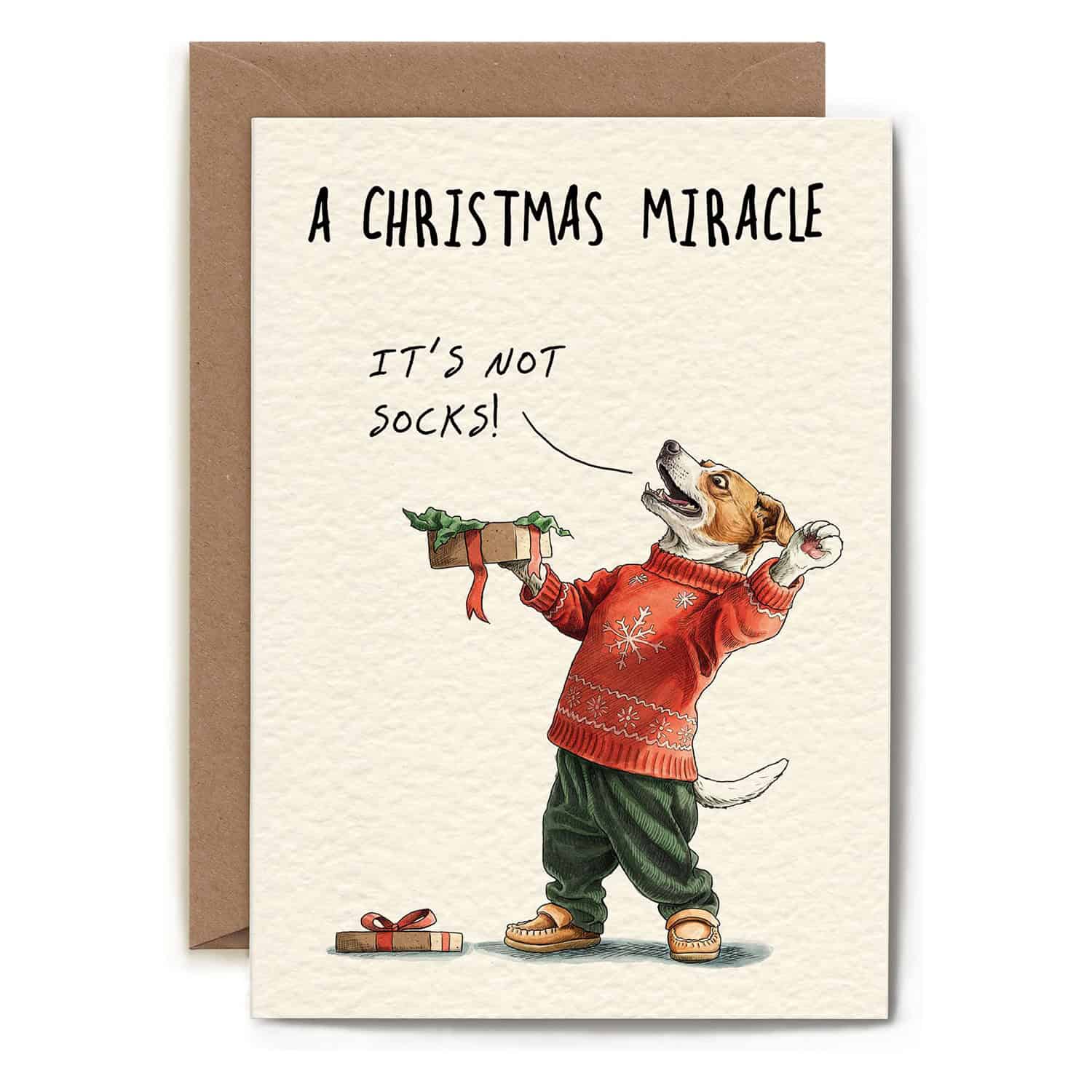 Christmas card with a dog in a sweater holding a gift, text 'A Christmas Miracle: It's not socks!' on a beige background.