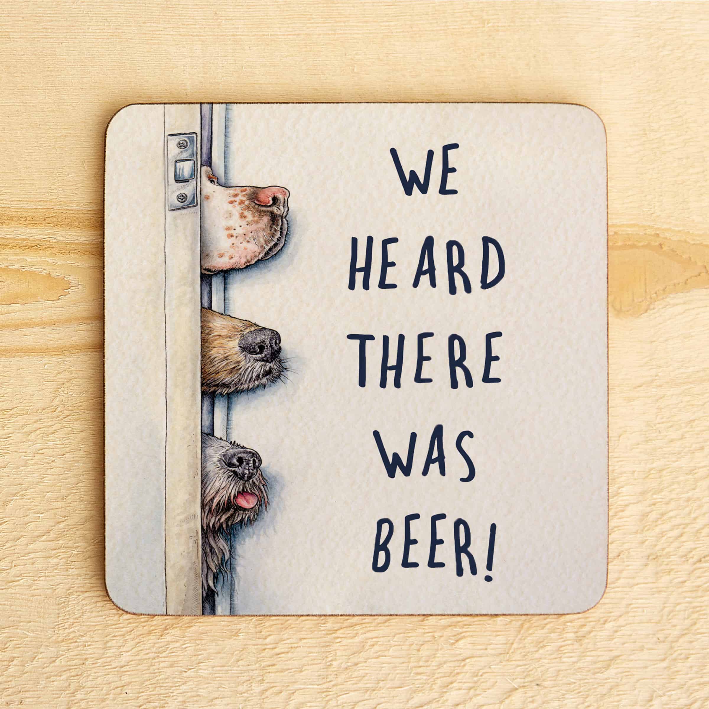 Coaster with illustration of dogs peeking around a door and text 'WE HEARD THERE WAS BEER!' on a wooden surface.