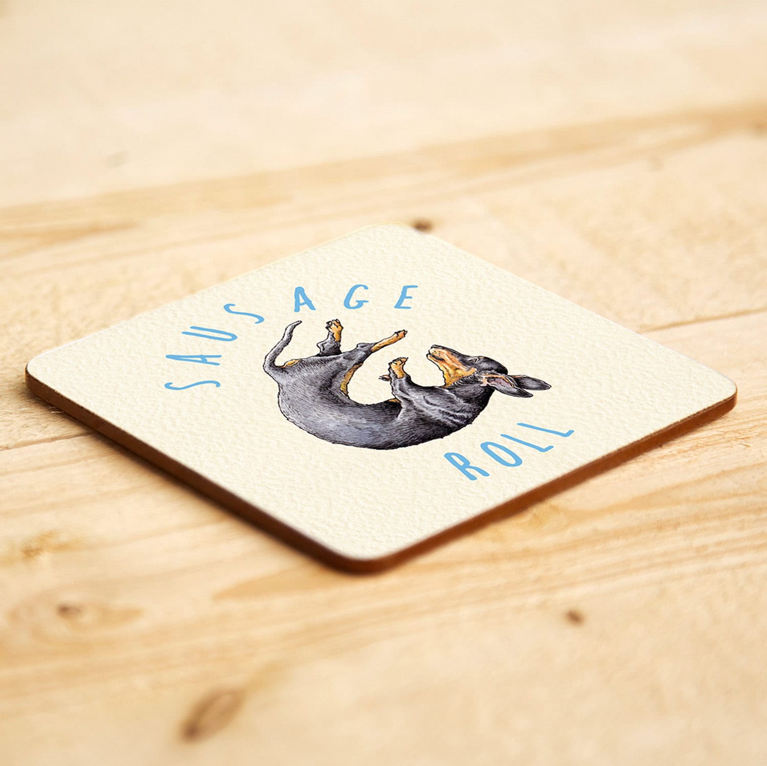 Coaster with a sausage dog illustration and 'Sausage Roll' text on a wooden surface