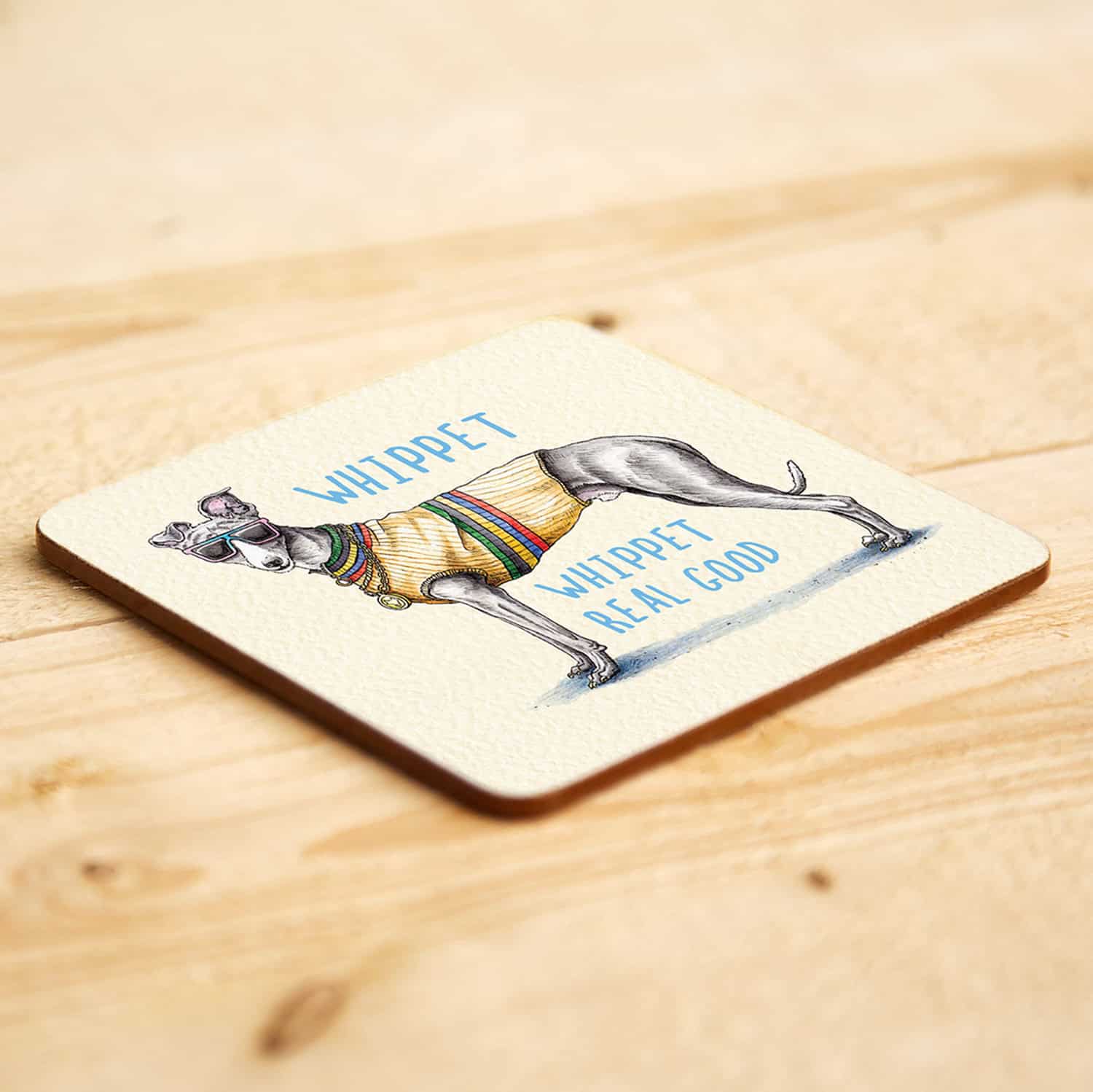 Coaster with a drawing of a whippet wearing sunglasses and a sweater, text 'WHIPPET WHIPPET REAL GOOD' on a wooden surface.
