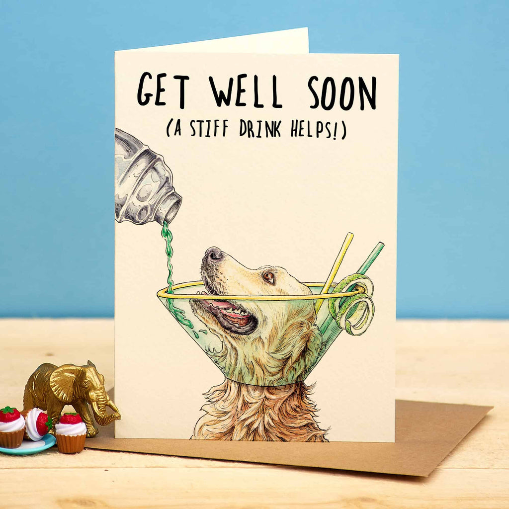 Get well soon card with a dog in a cone and drink, on a wooden surface with a blue background.