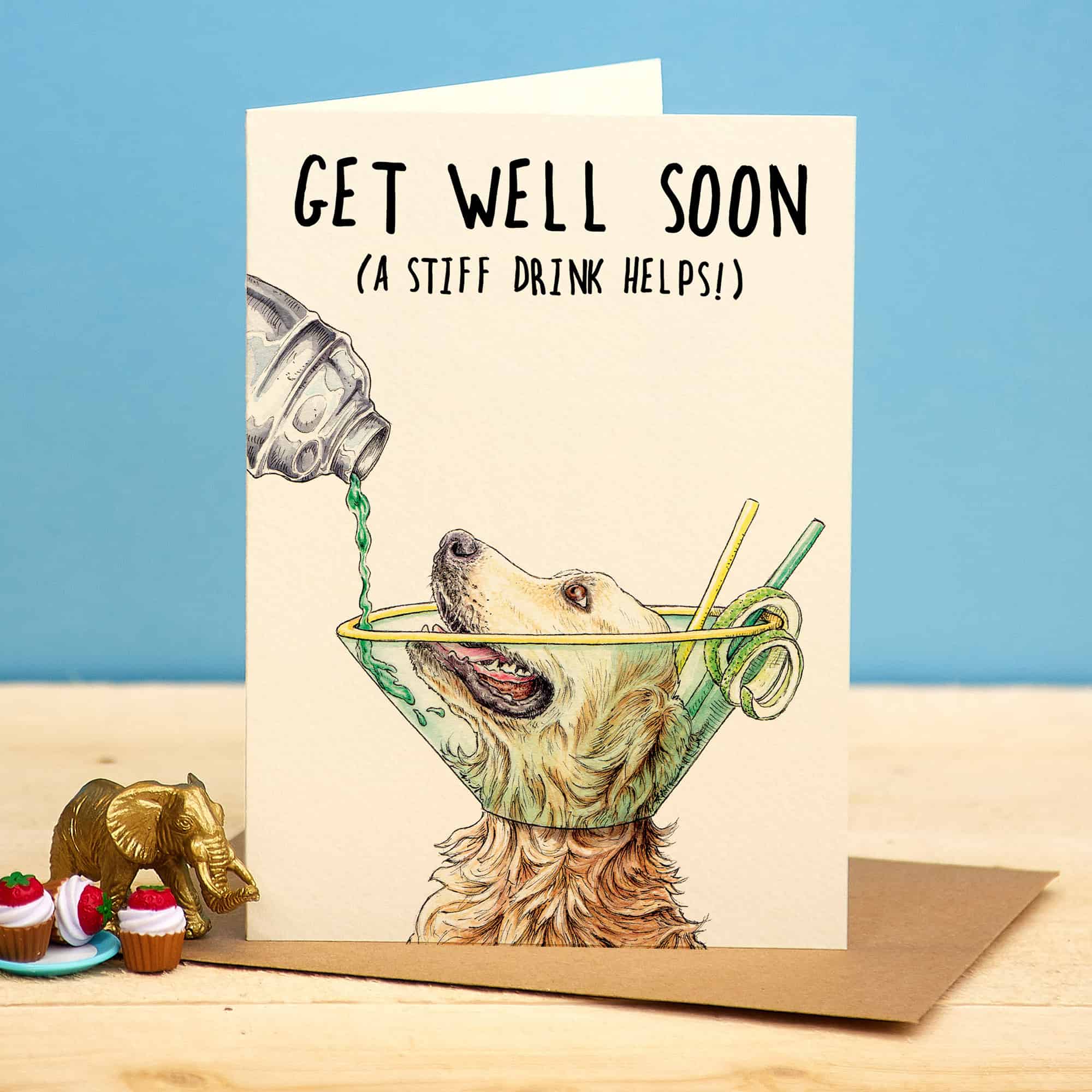 Get well soon card with a dog in a cone and drink, on a wooden surface with a blue background.