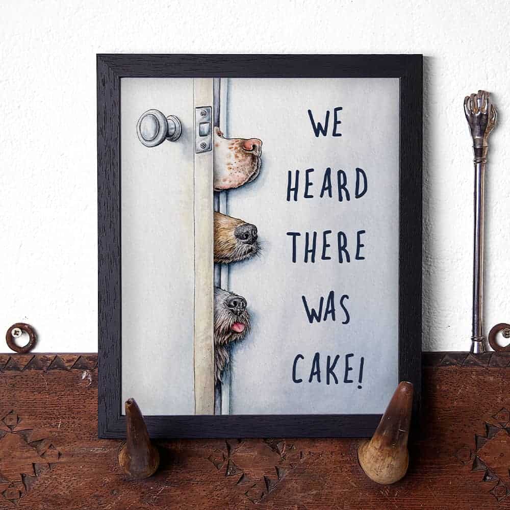 Artwork with dogs peeking around a door and text 'We heard there was cake!' on a wooden surface.