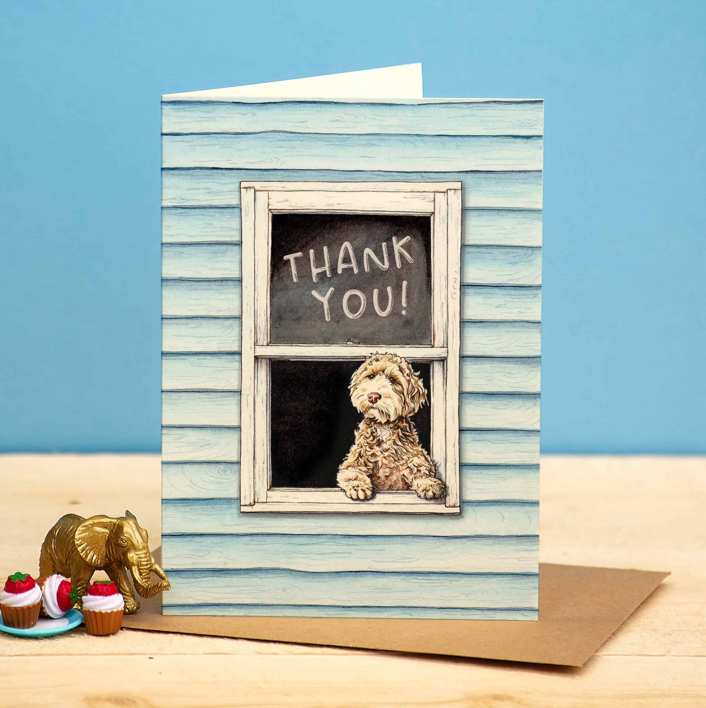 Greeting card with a dog looking out a window and 'Thank You!' on a chalkboard, with cupcakes and an elephant figurine on a blue and beige background.