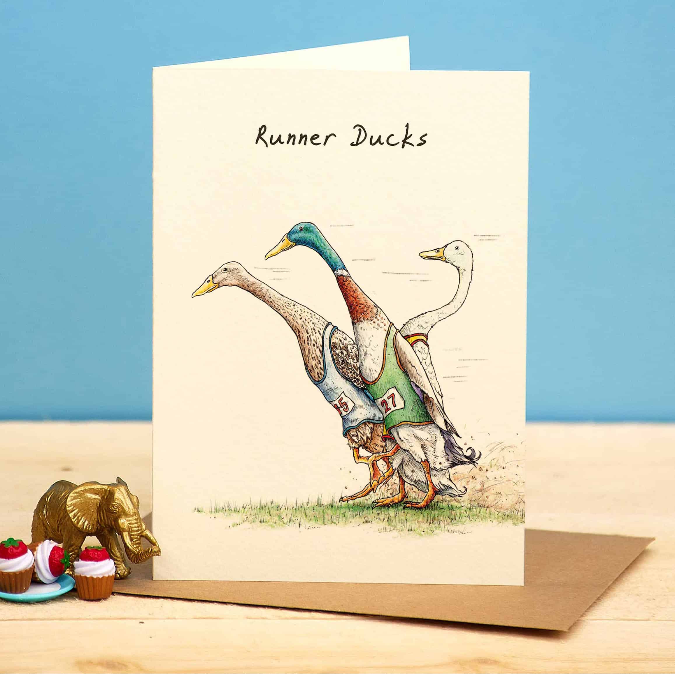 Greeting card with illustration of ducks in racing outfits on a wooden surface with a blue background
