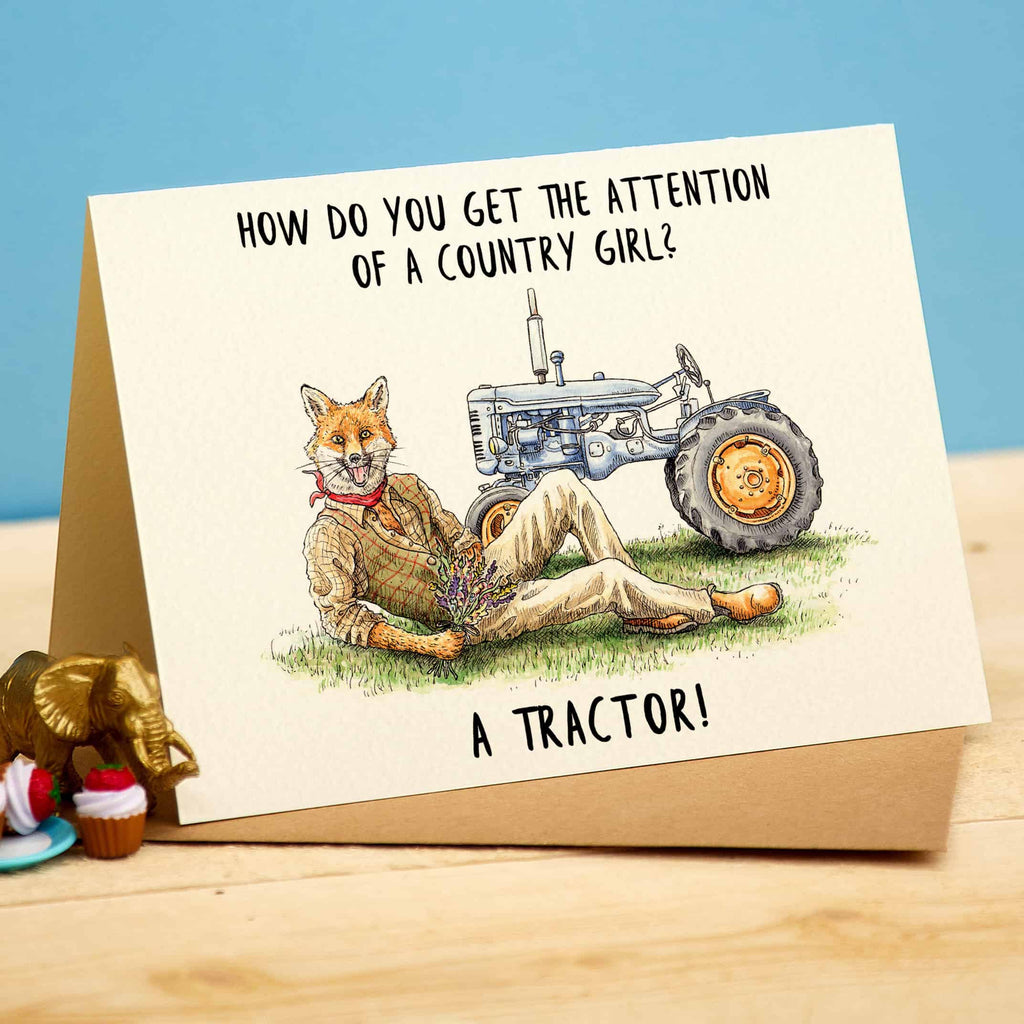 Card with a fox and tractor illustration and humorous text on a wooden surface.