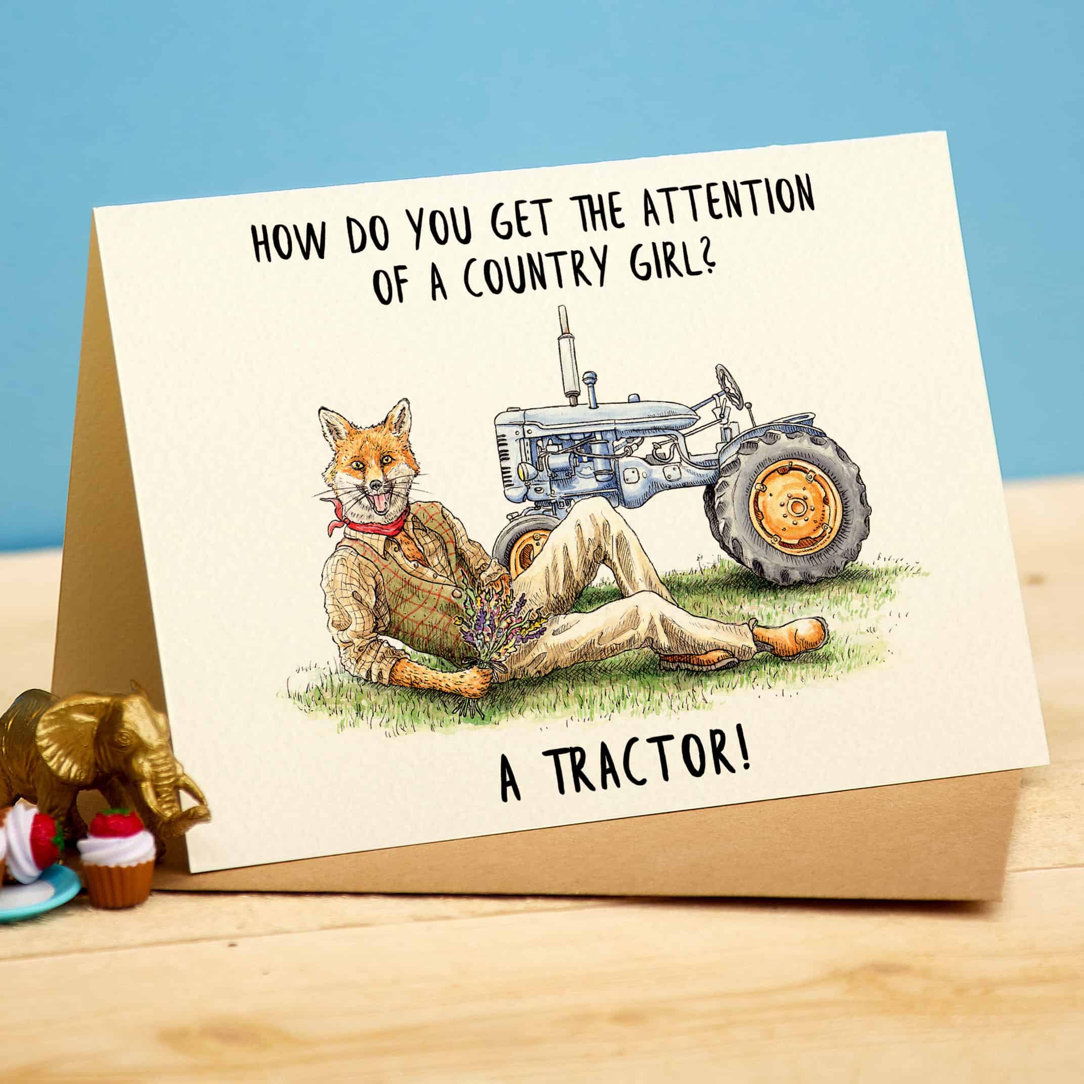 Card with a fox and tractor illustration and humorous text on a wooden surface.