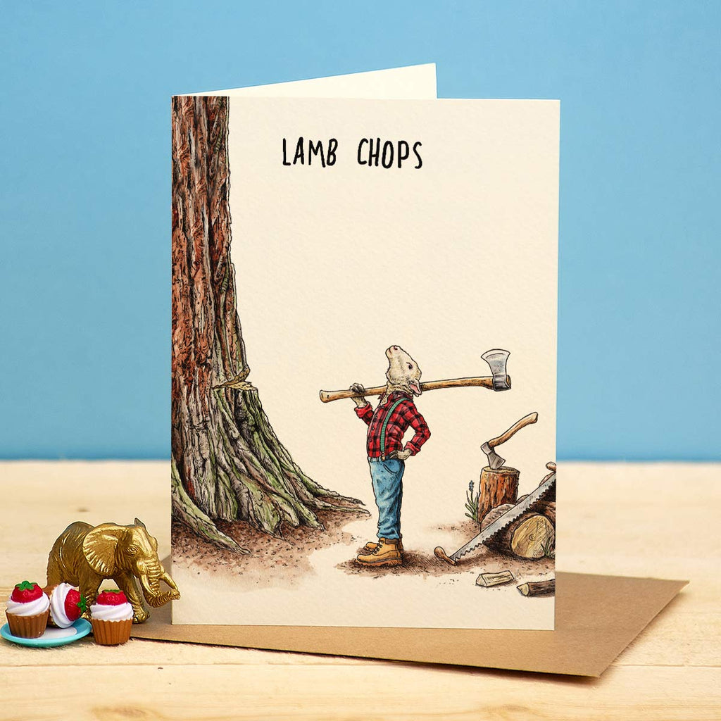 Greeting card with a bear holding a log over its shoulder, labeled 'Lamb Chops', on a wooden surface with a blue background.