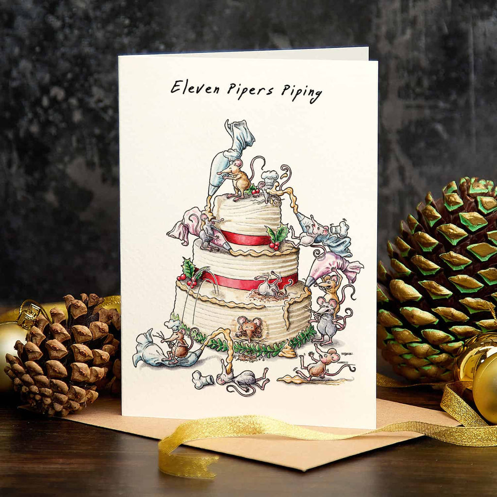 Card with a festive illustration of a wedding cake and pipers, surrounded by pine cones and gold ribbons.