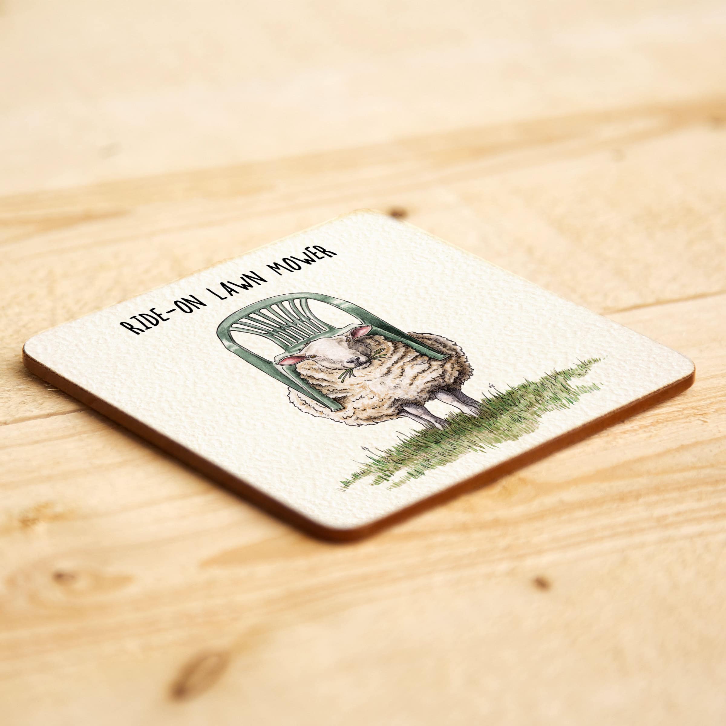 Coaster with a design of a sheep with a chair on top as a 'Ride-On Lawn Mower' on a wooden surface.
