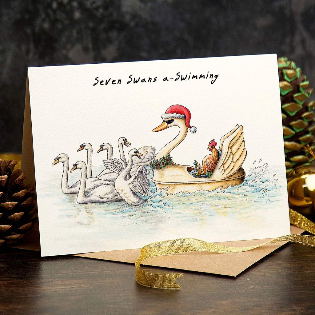 Christmas card with swans and a Santa-clad swan in a boat, surrounded by festive decorations.