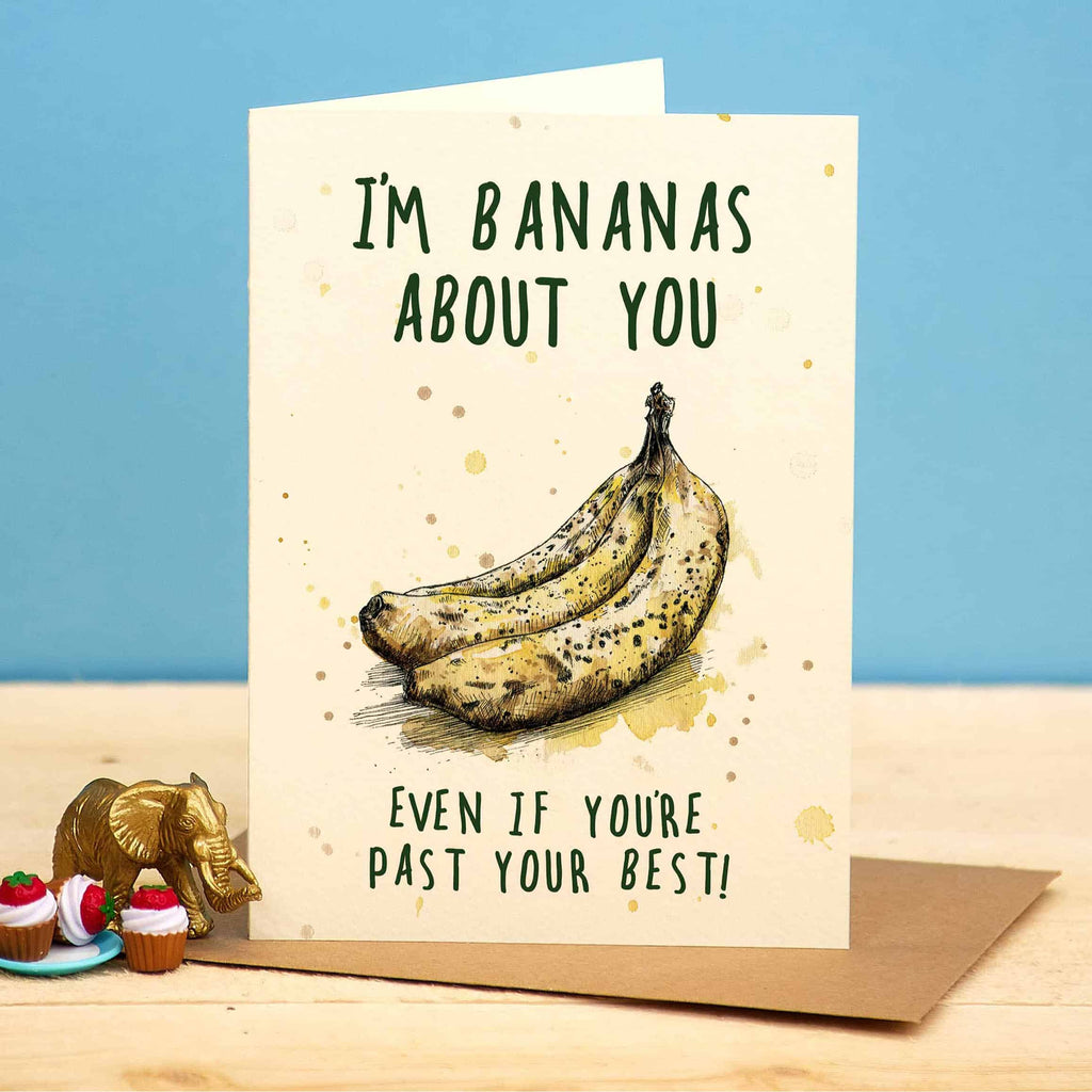 Card with bananas and text 'I'm bananas about you even if you're past your best!' on a wooden surface with a blue background.