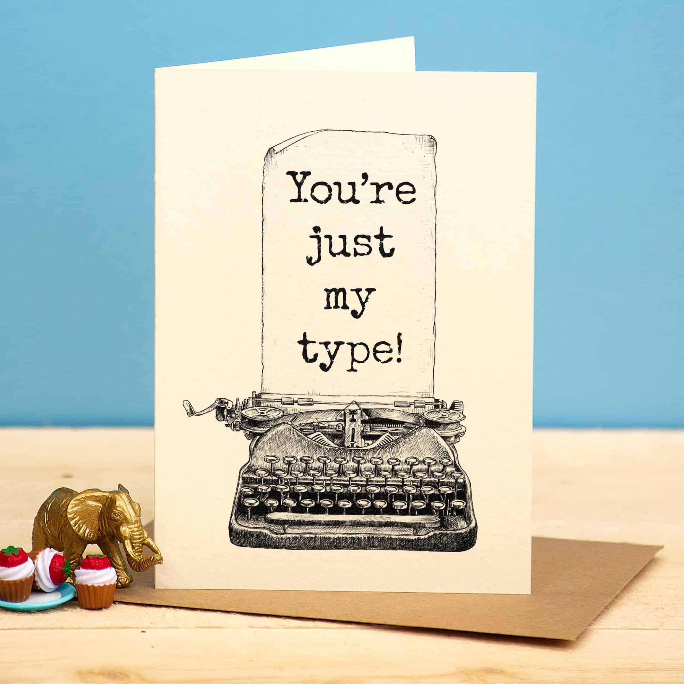 Greeting card with typewriter illustration and text 'You're just my type!' on a blue background.