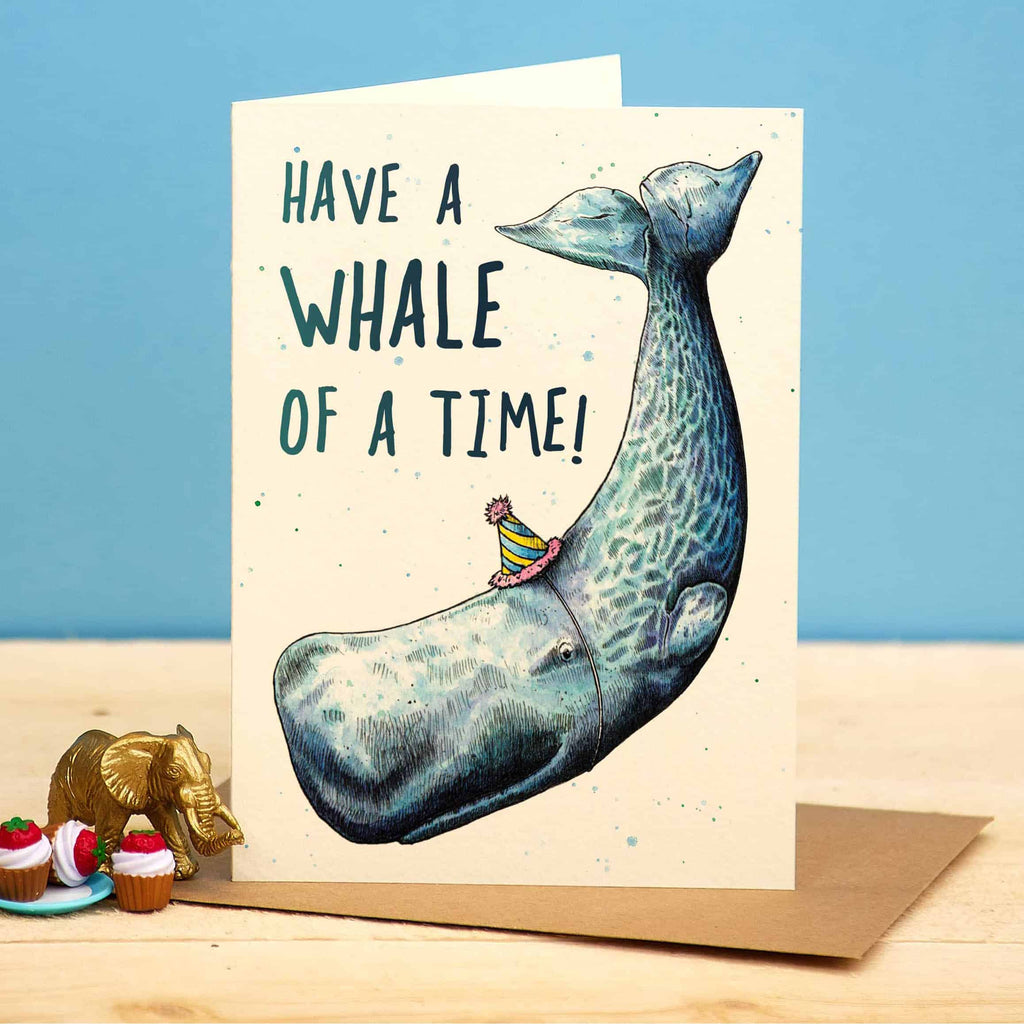 Greeting card with a whale illustration and text 'Have a whale of a time!' on a wooden surface.