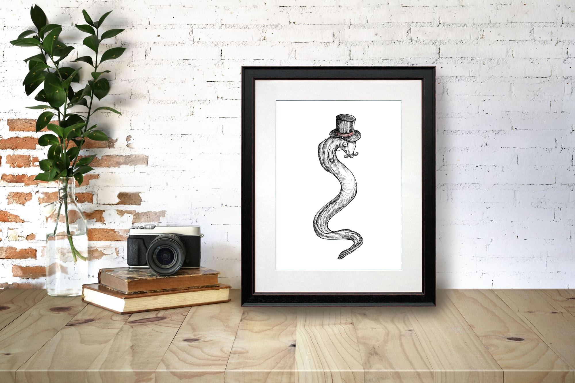 Black and white print of an eel wearing a top hat with the text “Genteel” in a black frame on a wooden desk