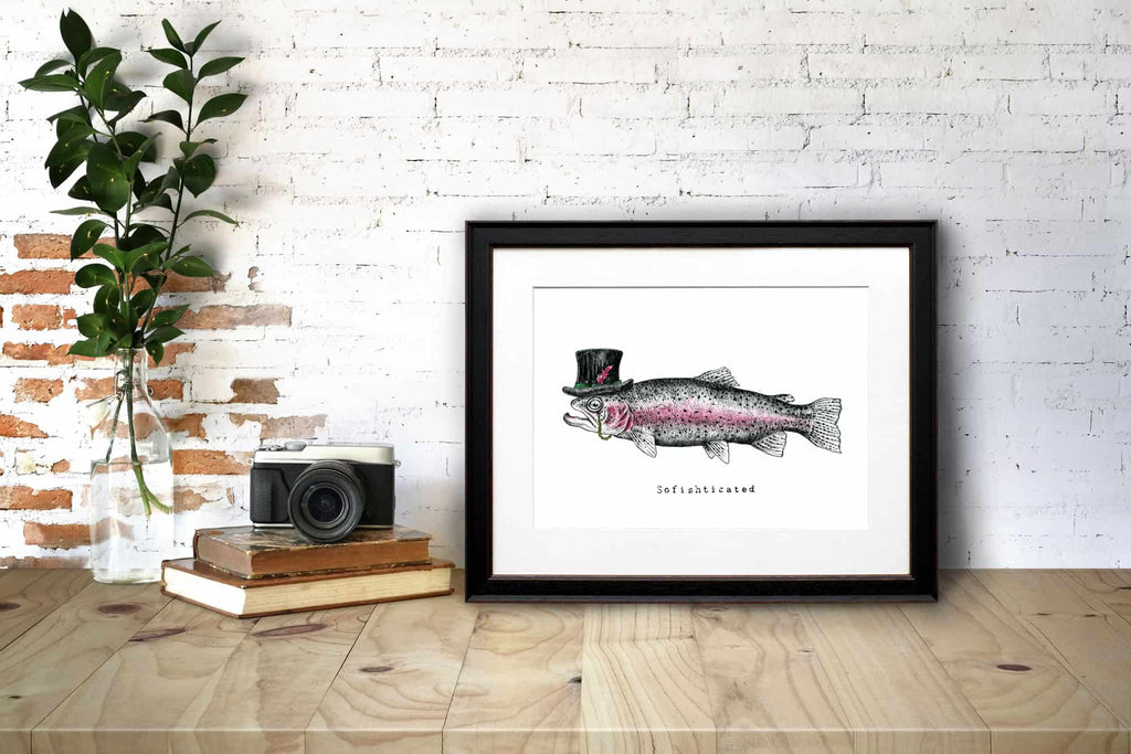 Print of a fish wearing a top hat with a monocle in a black frame on a wooden desk leaning against a white brick wall