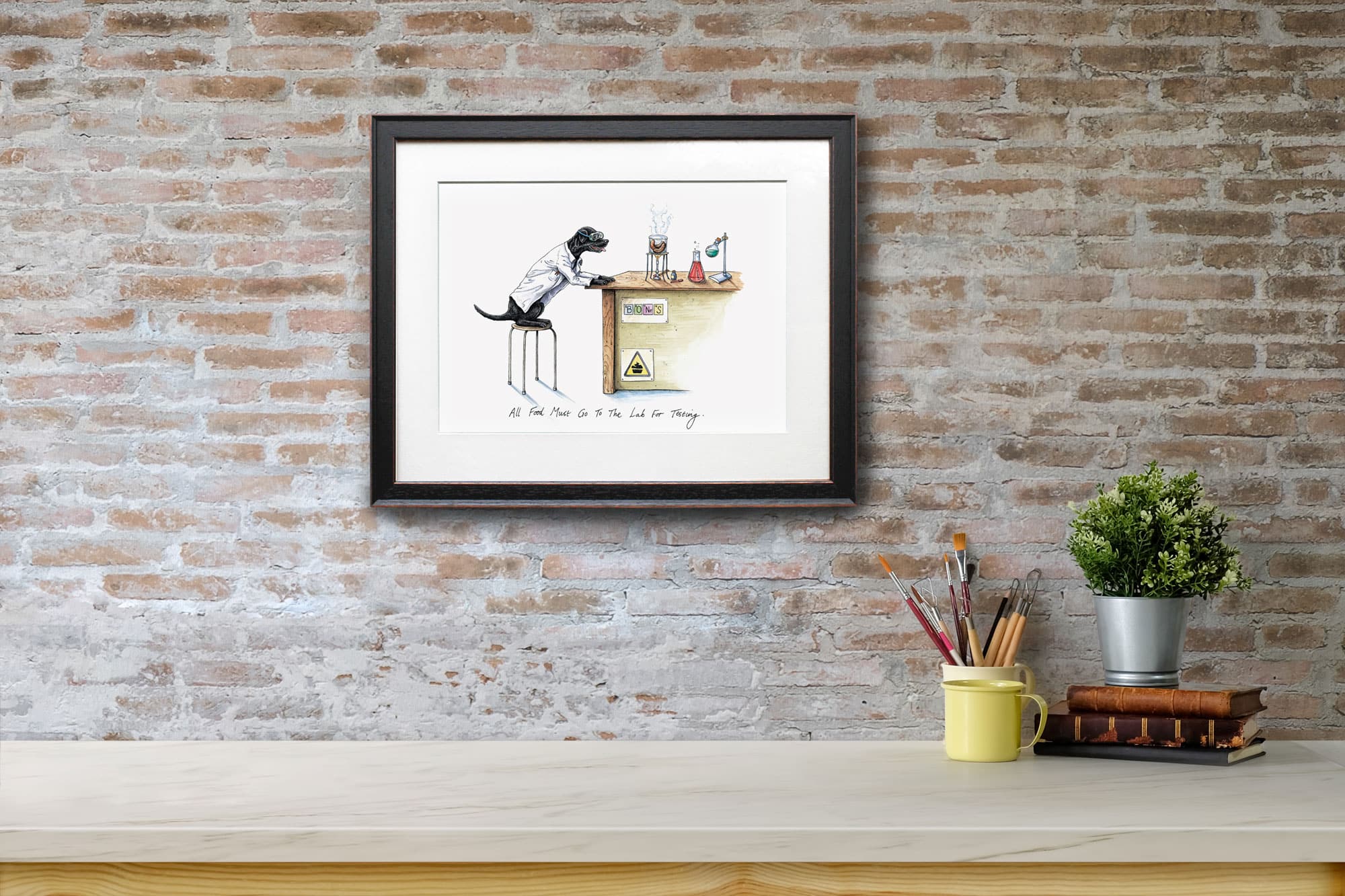 Print of a black labrador wearing a white Lab coat sitting at a desk in a science lab in a black frame on a red brick wall