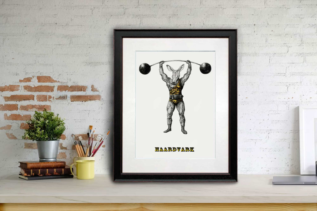 Print of an aardvark dressed as strong man wearing a leotard and lifting a barbell in a black frame sitting on a shelf