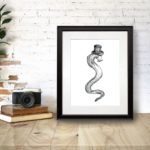 Black and white print of an eel wearing a top hat with the text “Genteel” in a black frame on a wooden desk
