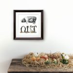 Print of a saddleback pig and lettering decorated with vegetables in a dark wood frame on a white wall above a wooden shelf