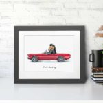 Print of a Mustang horse wearing a leather jacket driving a red ford mustang car in a grey frame sitting on a desk