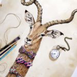 Head and neck of an impala which is wearing three very colourful decorative bow ties on a textured background